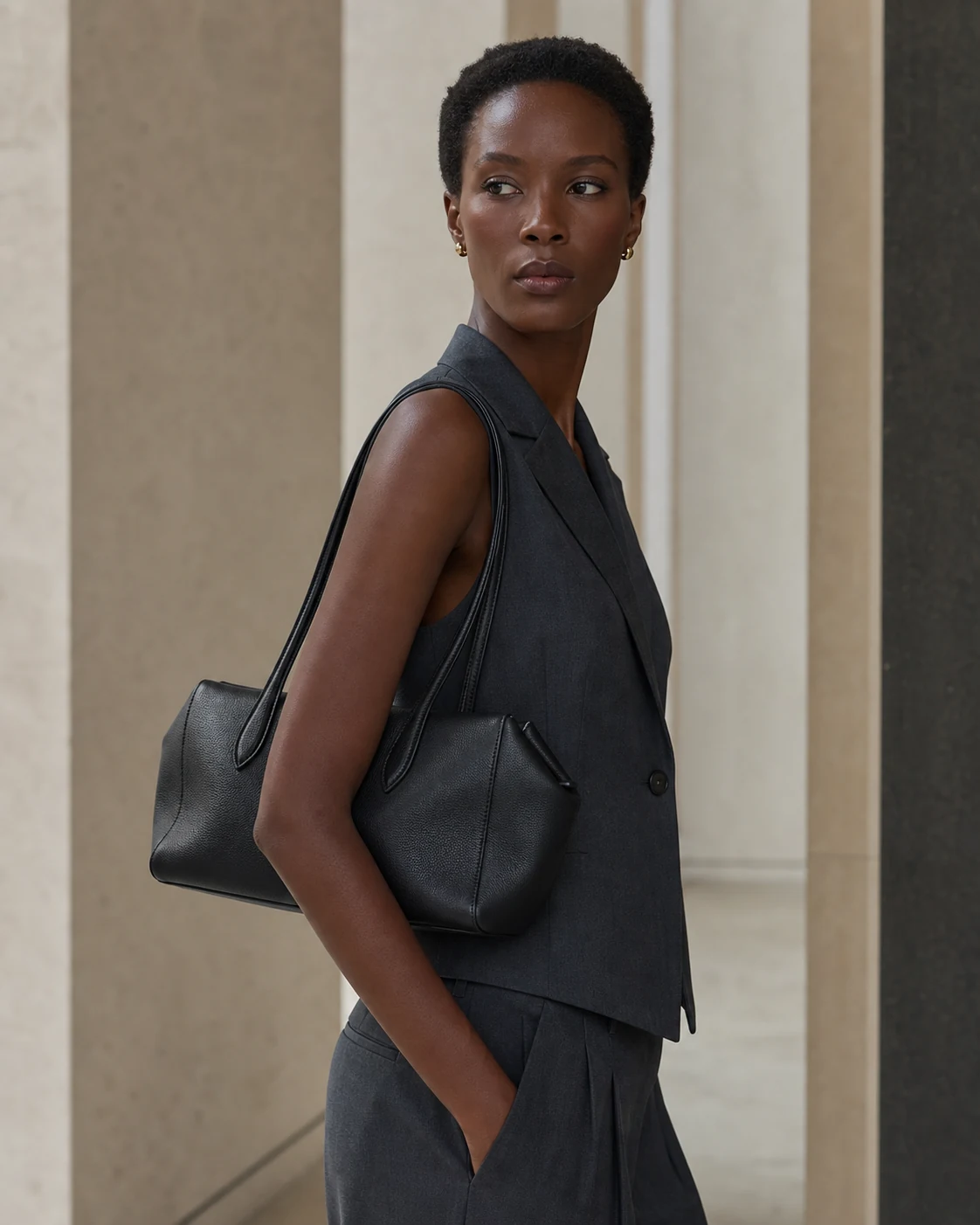 Black Camille Verve top-grain leather shoulder tote worn under the arm by a short-haired Black woman in a warm-gray gallery for the KOUSYN new arrivals campaign.